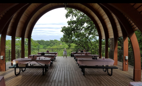 A spacious wooden pavilion with picnic tables overlooking a green landscape under a cloudy sky.