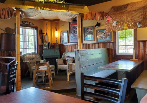 Cozy restaurant interior with bamboo decor, wooden tables, and seating areas, featuring warm lighting and tropical accents.