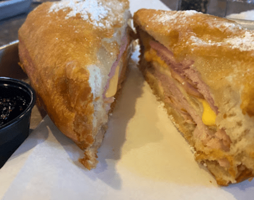 A close-up of a sliced sandwich with ham, cheese, and a golden crust, served with a side of jam.