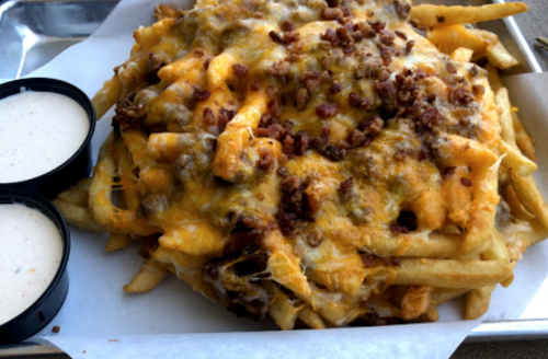 A large serving of loaded fries topped with cheese and bacon, served with two dipping sauces on the side.
