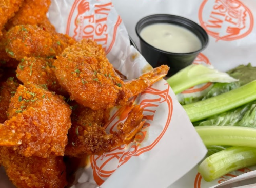 Crispy orange shrimp with a side of celery and dipping sauce in a takeout container.