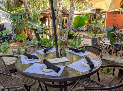 A cozy outdoor dining table set with black napkins and menus, surrounded by lush greenery and a relaxed atmosphere.