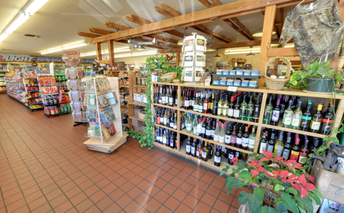 Interior of a store featuring shelves of wine, snacks, and drinks, with a cozy, rustic atmosphere.