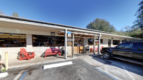 A storefront with large windows, red chairs outside, and a black truck parked nearby under a clear blue sky.