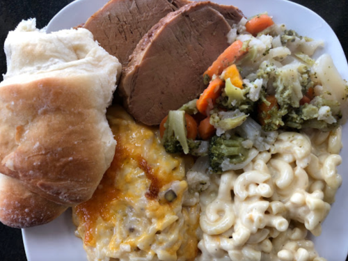 A plate of food featuring sliced meat, macaroni and cheese, mixed vegetables, a cheesy casserole, and a roll.