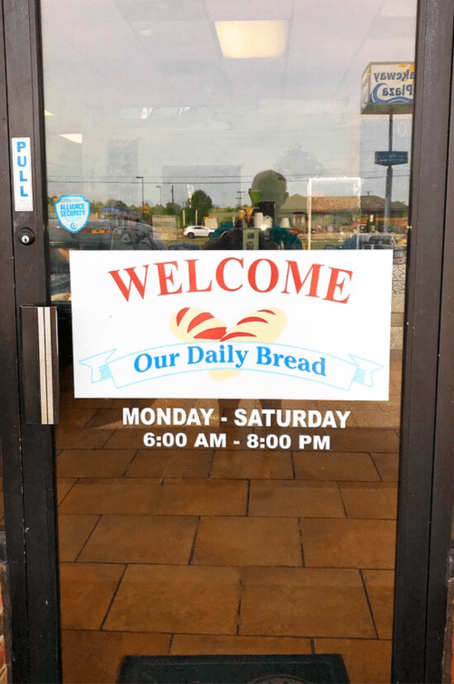 Sign on a glass door reading "Welcome Our Daily Bread" with hours: Monday-Saturday, 6:00 AM - 8:00 PM.