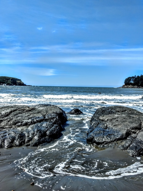 A rocky shoreline with gentle waves lapping against the stones under a clear blue sky.