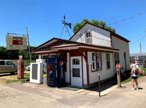 A small, vintage store with a Pepsi sign, featuring a soda machine and a stop sign outside on a sunny day.