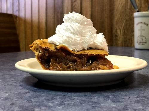 A slice of pie topped with whipped cream on a white plate, set against a wooden background.