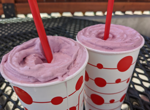 Two cups of purple frozen dessert with red straws, placed on a black metal table.