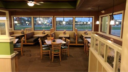 Interior of a restaurant featuring booths and tables, with large windows and warm lighting.