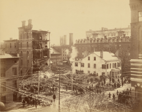 Historic photo of a building collapse, with crowds gathered and debris scattered in a city setting.