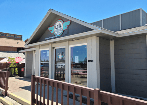 Exterior of a restaurant named "i.d.k." with a sign and large windows, surrounded by a wooden railing and blue sky.