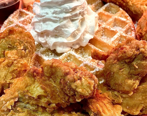 A plate featuring crispy fried chicken served with a golden waffle topped with whipped cream.