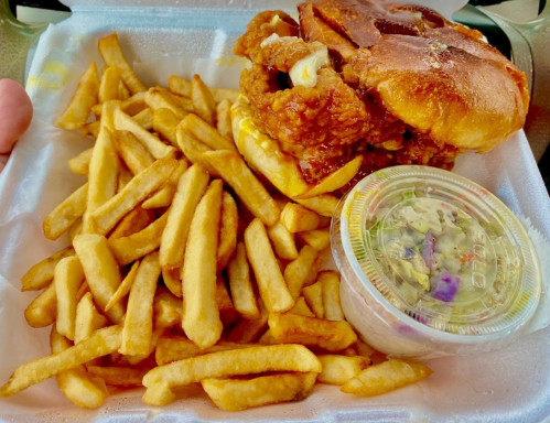 A takeout container with a fried chicken sandwich, fries, and a small cup of coleslaw.