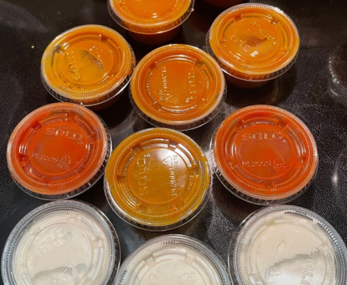 A collection of small plastic containers filled with various sauces, arranged on a dark surface.