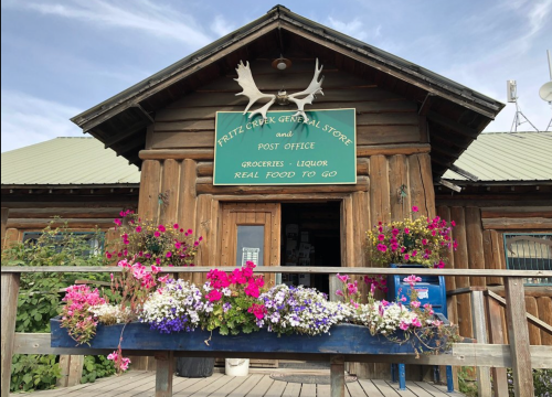 A rustic wooden general store with a sign for groceries and liquor, adorned with colorful flower boxes.