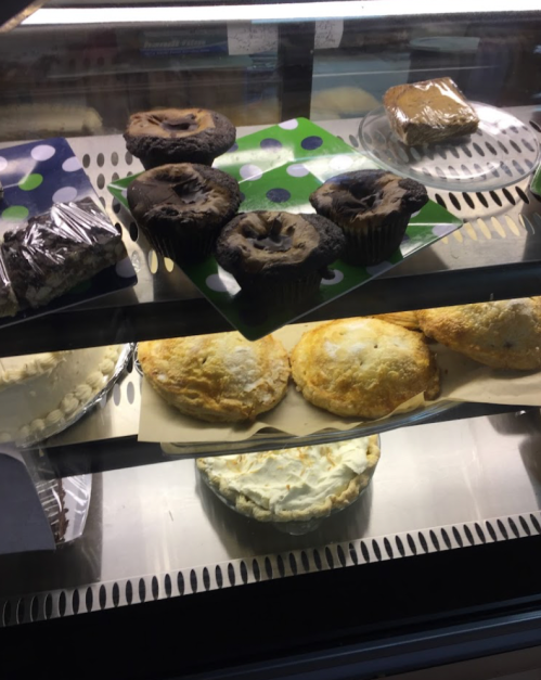 A display case filled with various baked goods, including muffins, pies, and a cake.