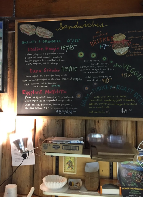 Chalkboard menu displaying sandwich options and prices, including hoagies, grinders, and muffuletta.