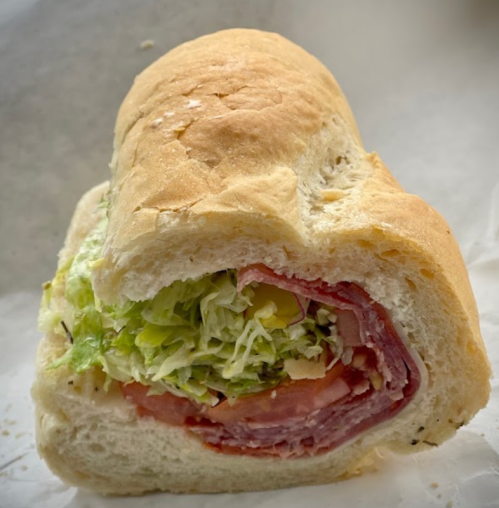 A close-up of a sandwich with layers of lettuce, tomato, and deli meats, served in a soft, crusty bread roll.