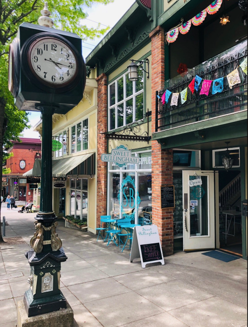 A charming street scene featuring a vintage clock, colorful decorations, and a shop entrance with outdoor seating.