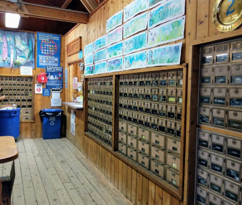 Interior of a wooden building featuring mailboxes, bulletin boards, and colorful artwork on the walls.