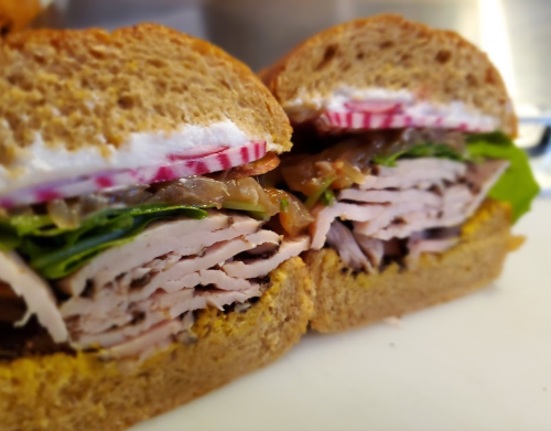Close-up of a sliced sandwich with turkey, lettuce, radish, and mustard on whole grain bread.