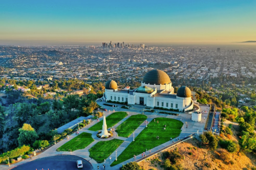 Aerial view of the Griffith Observatory with Los Angeles skyline in the background during sunset. Green park area in foreground.