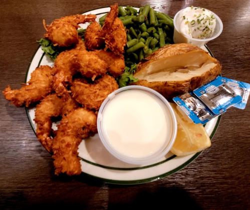 A plate of fried shrimp, green beans, a baked potato, and dipping sauce, garnished with a lemon wedge.