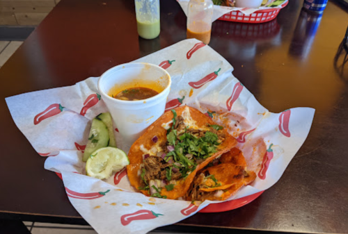 A plate of tacos with meat, topped with cilantro and onions, served with a side of lime and a cup of broth.