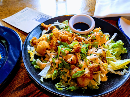 A plate of crispy fried cauliflower on a bed of lettuce, drizzled with sauce and sprinkled with sesame seeds.