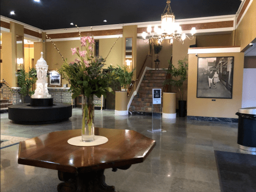 A spacious lobby with a floral arrangement, a statue, and a staircase, featuring elegant decor and plants.