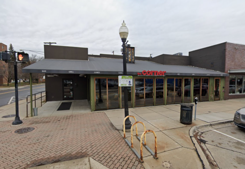 Exterior view of a restaurant called "The Corner," featuring large windows and a sidewalk with bike racks.