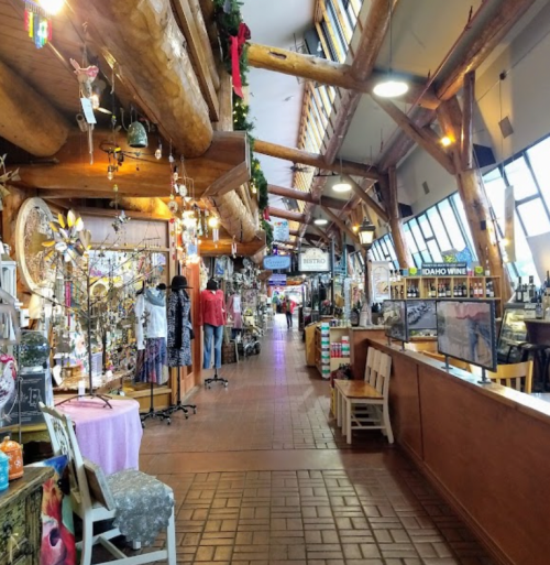 A vibrant indoor market with wooden beams, showcasing various shops, crafts, and decorations along a spacious walkway.