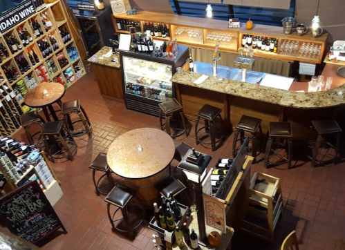 A cozy wine bar with wooden tables, a counter, and shelves filled with various wine bottles. Warm lighting creates an inviting atmosphere.