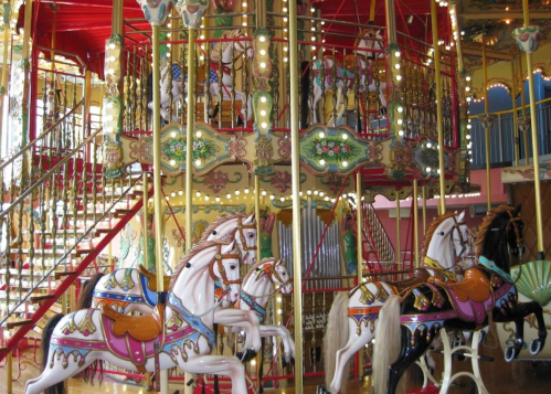 A colorful carousel with ornate horses and vibrant decorations, featuring multiple levels and bright lights.