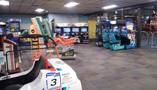 A colorful arcade with various vintage video game machines and racing simulators in a spacious room.