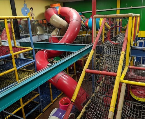 Colorful indoor play structure with slides, climbing nets, and tunnels for children.