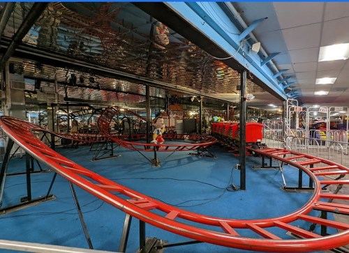 An indoor amusement park featuring a red roller coaster track with empty seats and a blue floor.