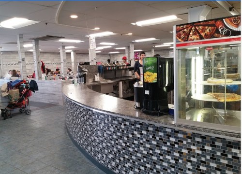 A busy food court with a curved counter, a drink dispenser, and a display of food items in a casual dining setting.