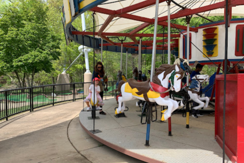 A carousel with colorful horses, featuring children and adults enjoying a sunny day at an amusement park.
