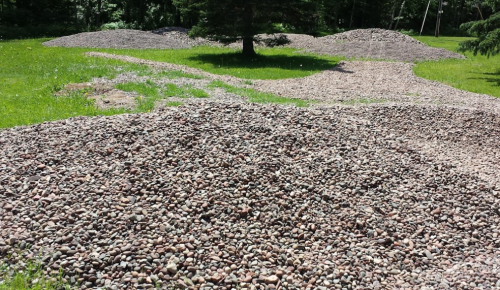 A landscape featuring several mounds of smooth stones surrounded by green grass and trees.