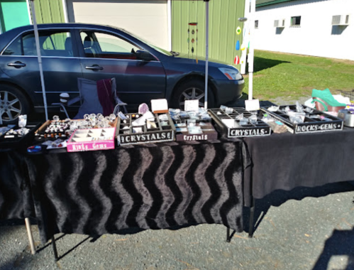 A market stall displaying various crystals and gemstones on a black tablecloth, with a car parked in the background.