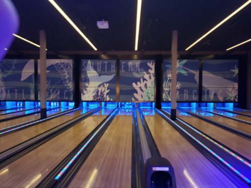 Bowling alley with illuminated lanes and ocean-themed murals in the background.