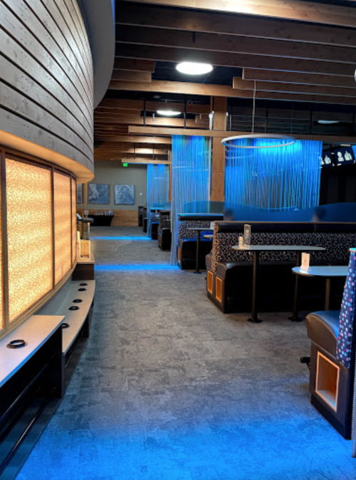 Modern restaurant interior with blue lighting, wooden beams, and cozy seating along a spacious corridor.