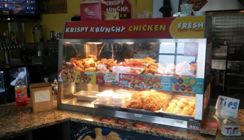 Display case filled with crispy fried chicken and sides at a fast-food restaurant, with a colorful sign above.