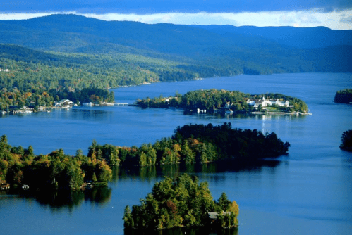 A scenic view of a lake surrounded by lush green islands and mountains under a partly cloudy sky.