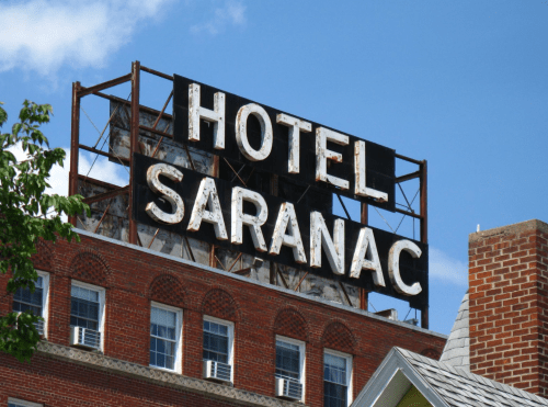 Sign for Hotel Saranac on a brick building, with a blue sky and clouds in the background.