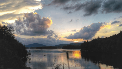 A serene lake at sunset, with colorful clouds reflecting on the water and mountains in the background.