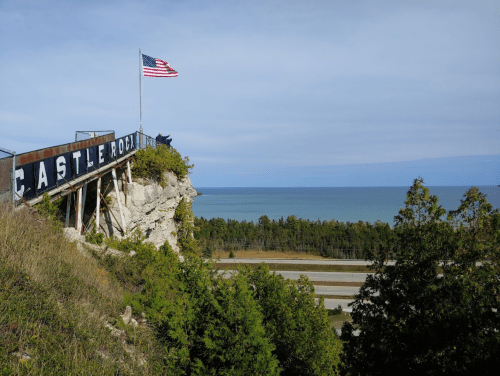 View from Castle Rock, featuring an American flag, rocky cliffs, and a serene lake in the background.